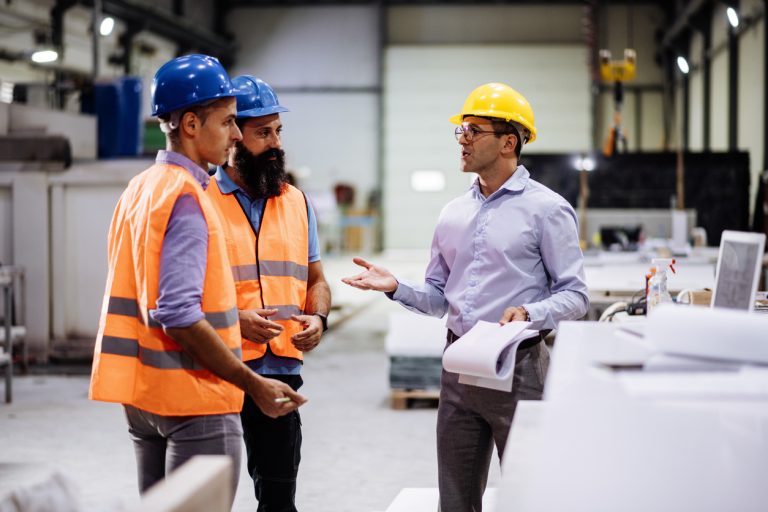 Engineers in factory hall, performing quality control. Manufacturing occupation in modern industrial hall, with automated process and robots. Metal processing industry and warehouse.