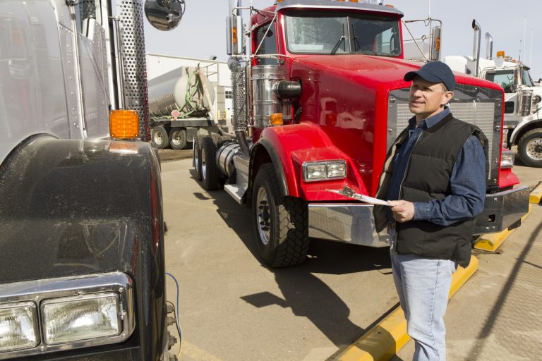 An image from the transportation industry of a truck driver at a truck stop doing a safety check on his vehicle.