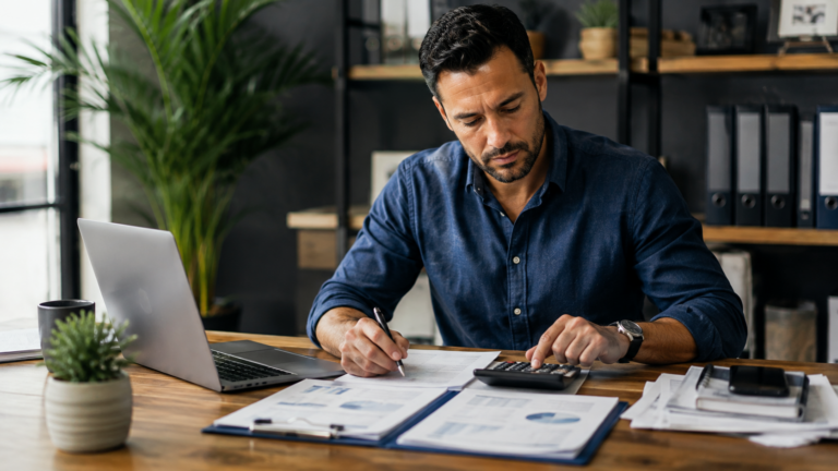 A business owner reviewing workers' compensation costs with a calculator and payroll